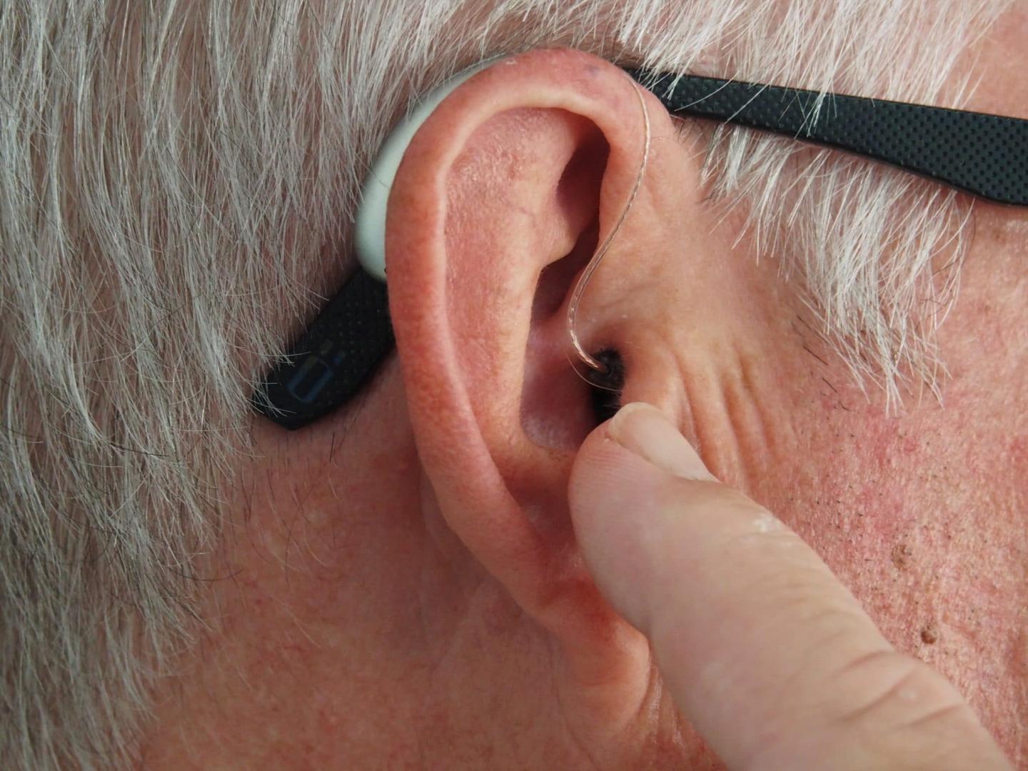 How Often Should You Wear Hearing Aids? Man points at his hearing aid