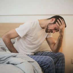 Tired man sitting on edge of bed.