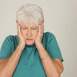 Older woman with hands covering her ears.