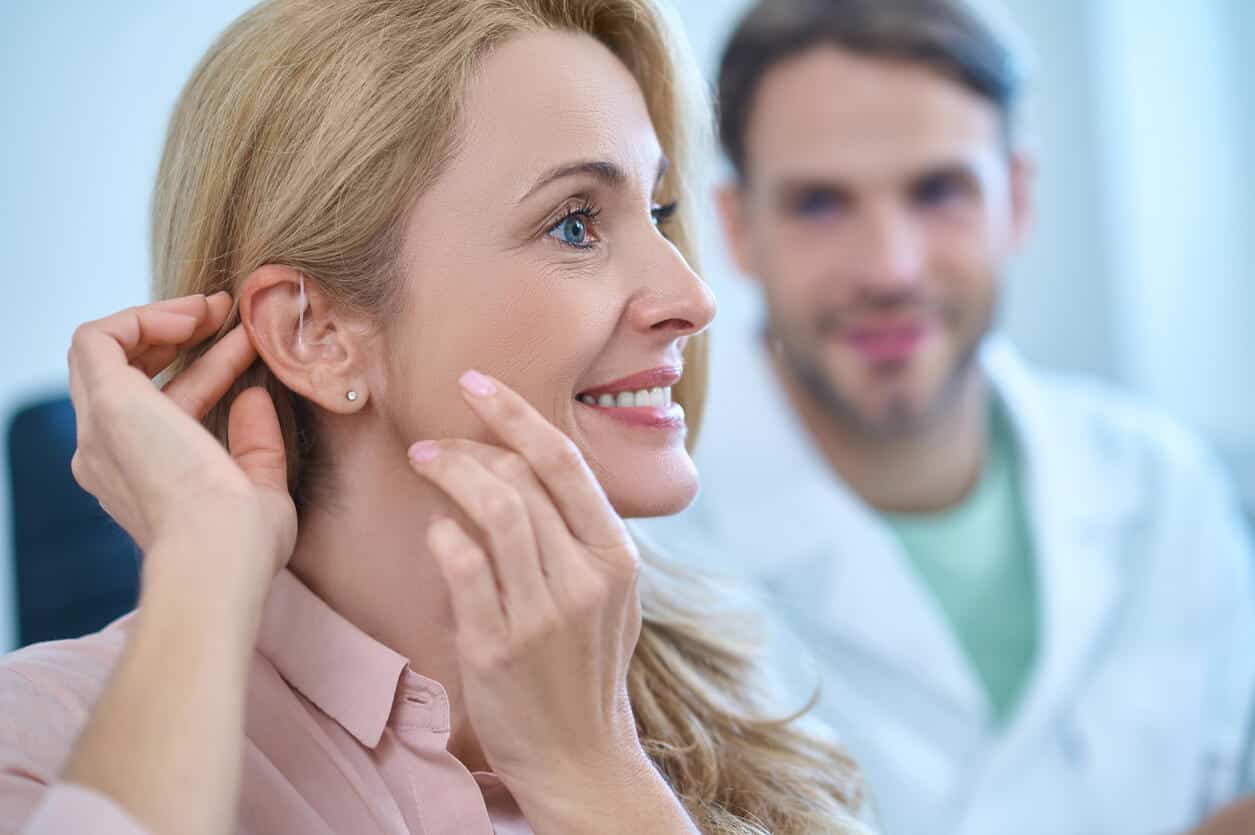 Woman adjusts hearing aids behind ear