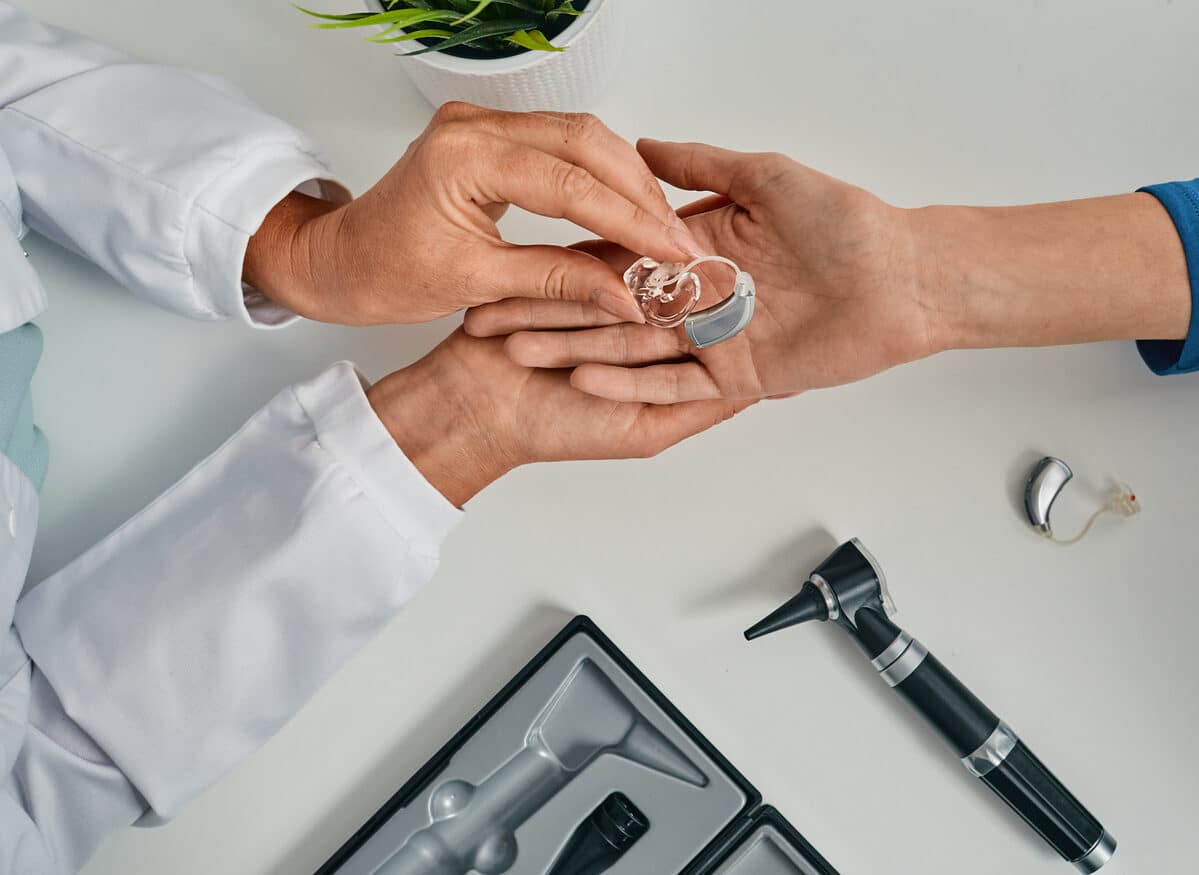 Audiologist hands the patient their new hearing aids over a table with hearing instruments.