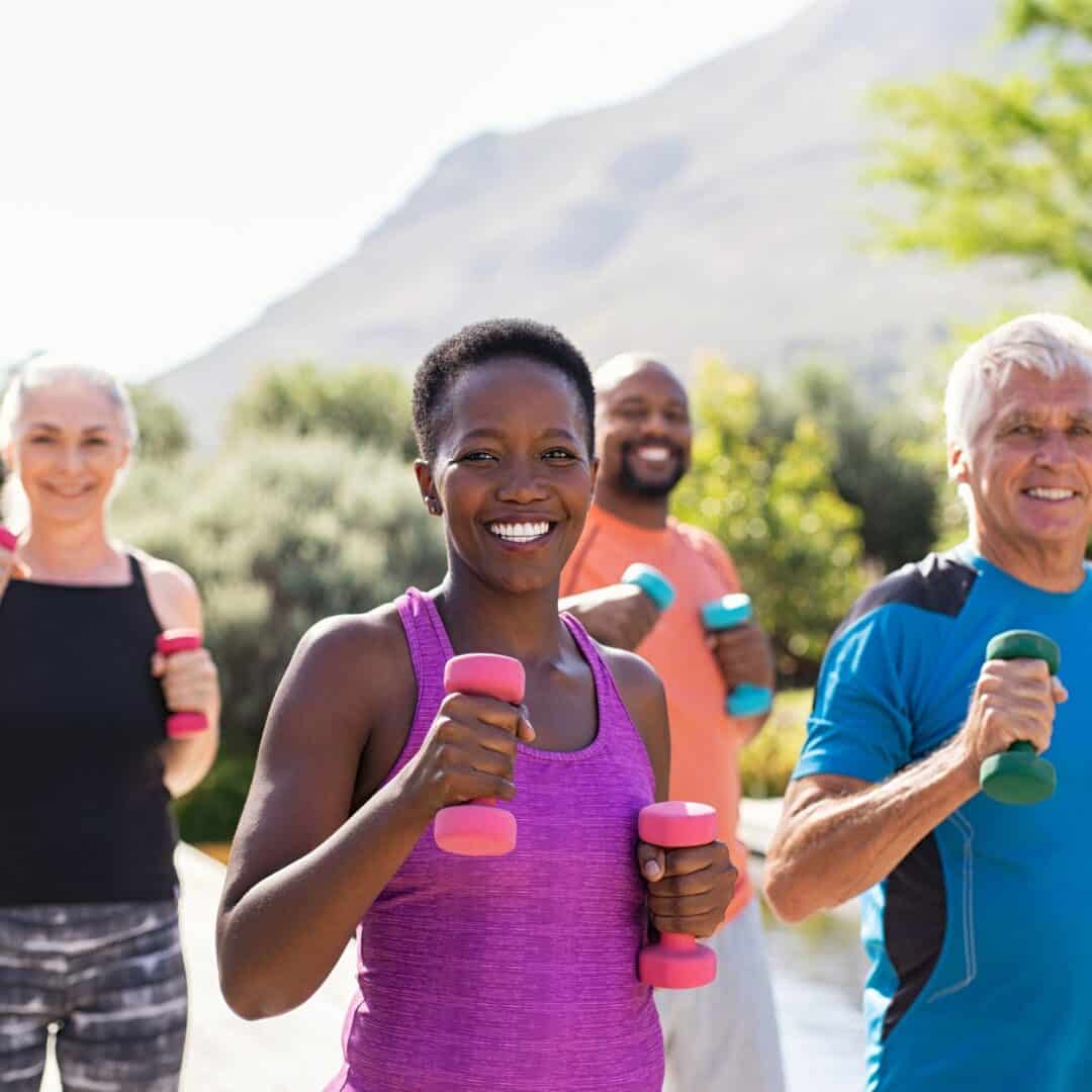 Outdoor fitness class with people using dumbbells and smiling.
