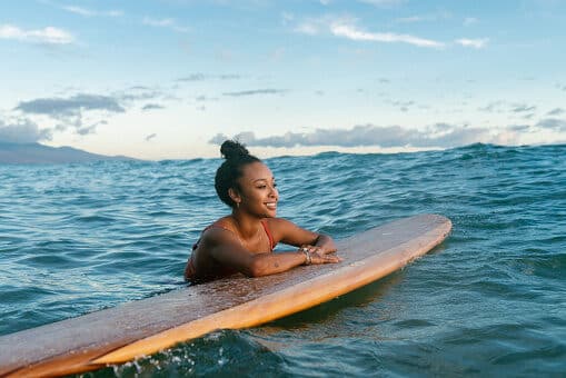 Surfer resting on her board between waves and smiling in the middle of the ocean