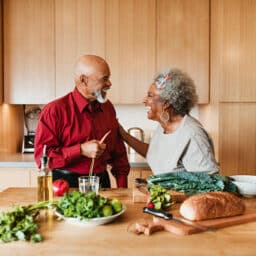 Happy older couple prepares a healthy dinner in their home kitchen, smiling and laughing together.