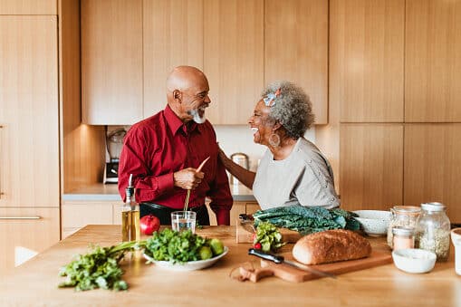 Happy older couple prepares a healthy dinner in their home kitchen, smiling and laughing together.