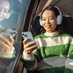 Woman on a train listening to music on her phone through over-ear headphones.