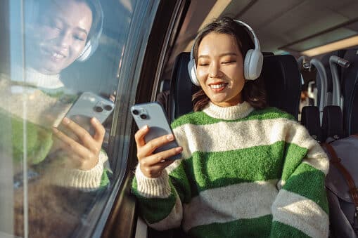 Woman on a train listening to music on her phone through over-ear headphones.