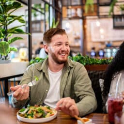 Smiling man eating a healthy salad at a restaurant with his friends.