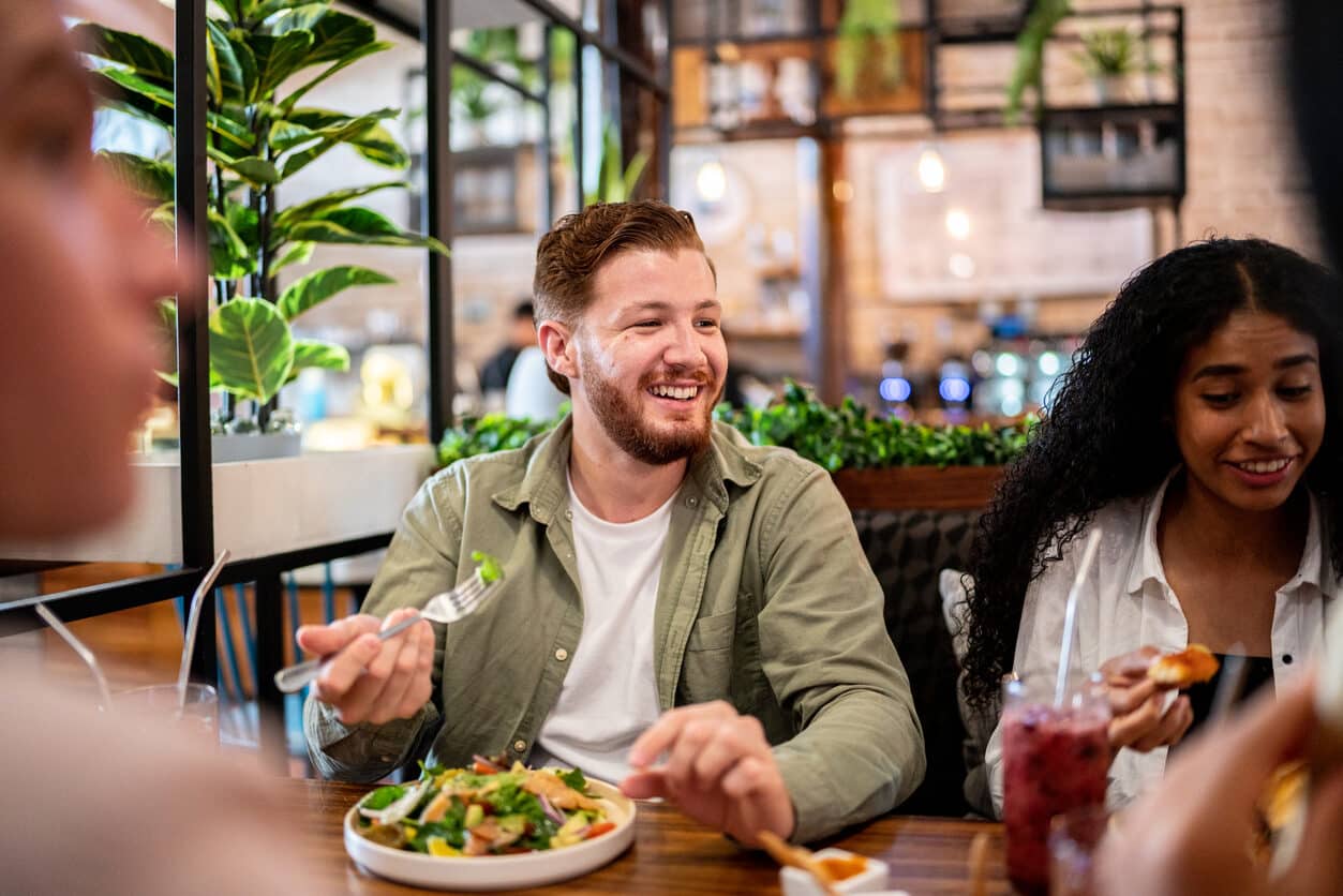 Smiling man eating a healthy salad at a restaurant with his friends.