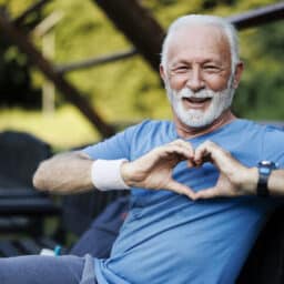 Portrait of a senior sporty man in nature showing a heart-shaped symbol